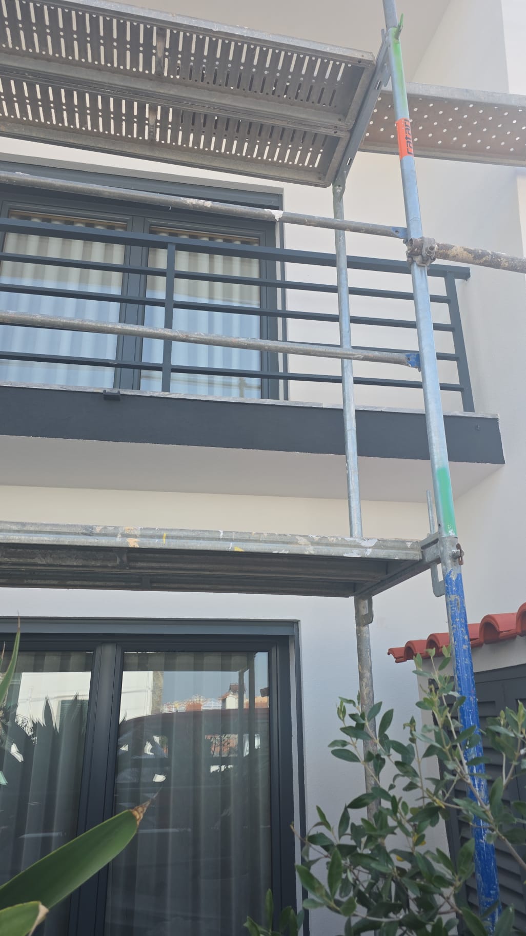 Varanda de moradia com guarda em ferro pintado a cinza-grafite, andaime montado durante o acabamento da fachada